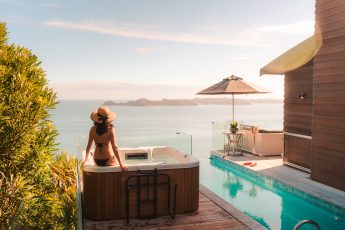 Guests enjoying the view over Long Beach and the Pacific Ocean from the spa at Cloud 9, Bay of Islands, New Zealand